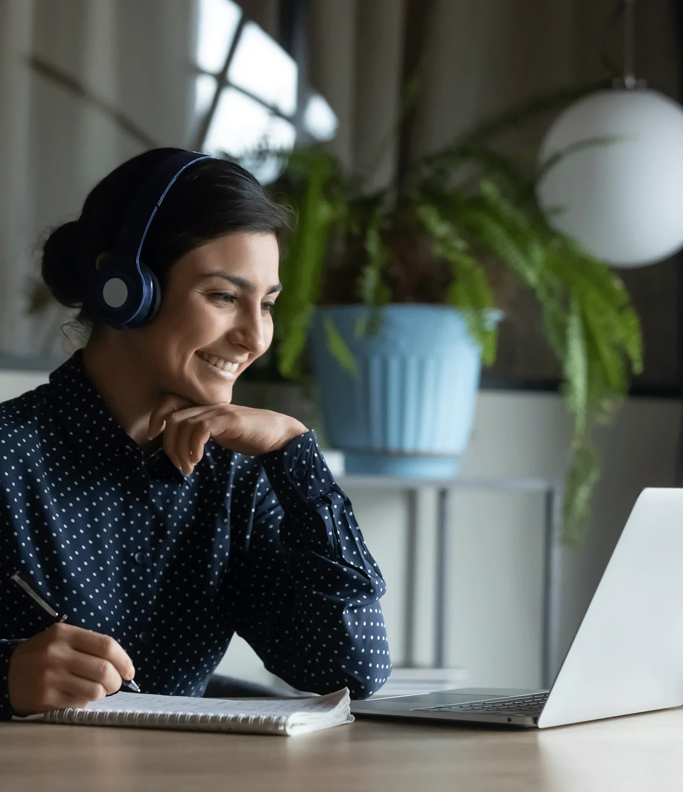 Frau sitzt mit Kopfh&ouml;rern vor einem Laptop und notiert etwas