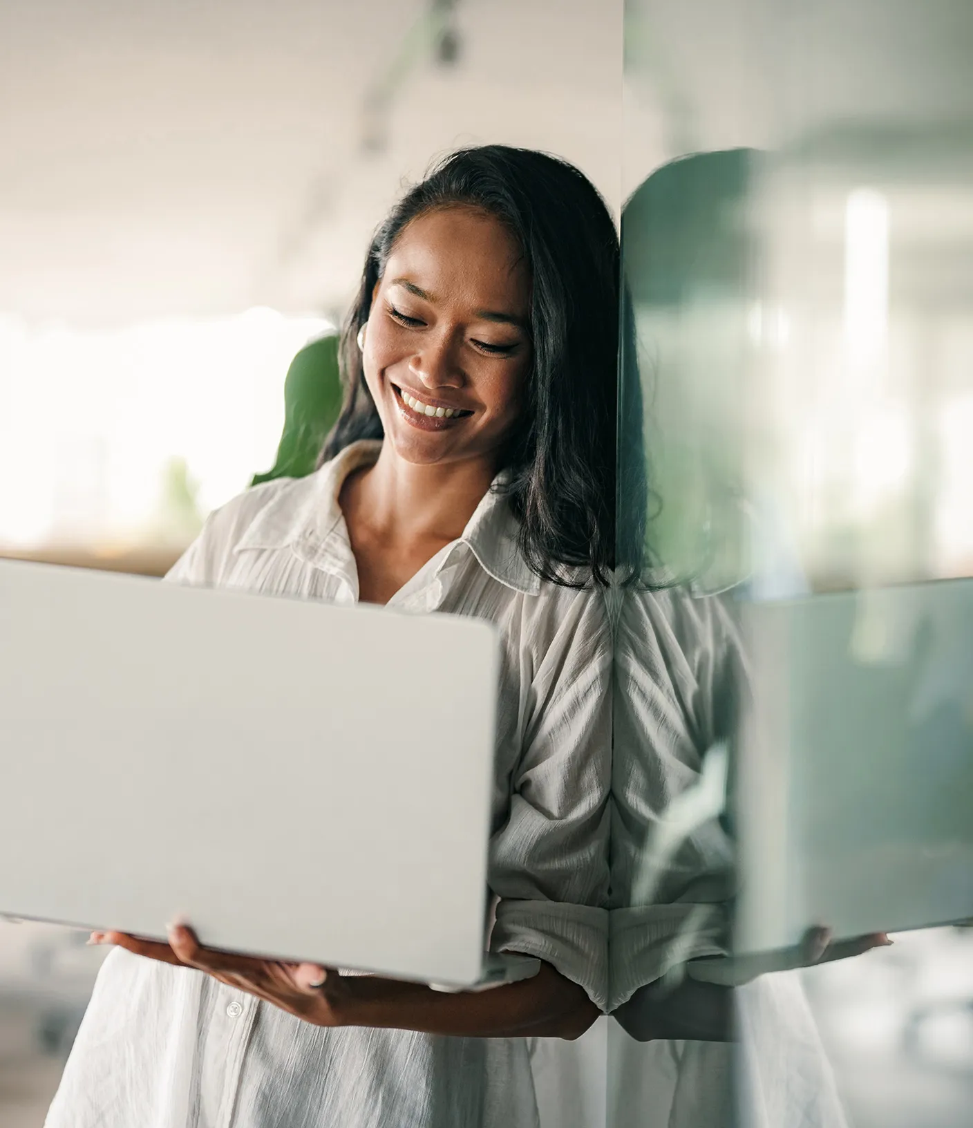 Frau mit Laptop in der Hand lehnt an einer Glaswand